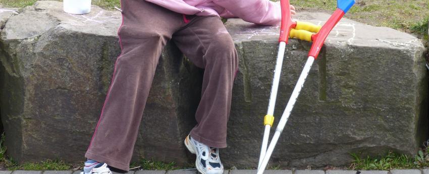 Niño/a con discapacidad sentado/a. A su lado hay unas muletas.