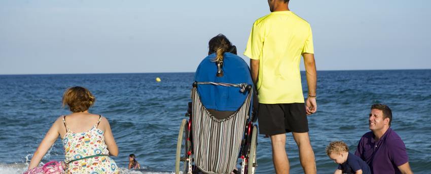 Un assistent personal acompanyant l'usuària que atén en una trobada amb amics a la platja