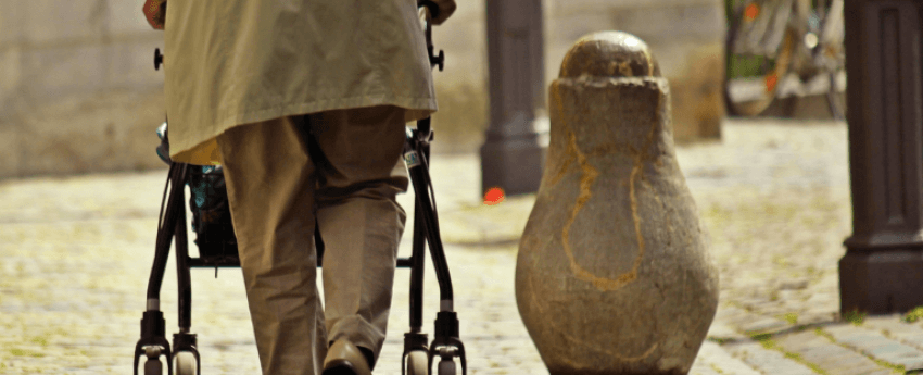 persona d'esquenes caminant pel carrer amb el suport d'un caminador