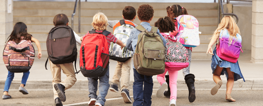 Grup de nens d'esquenes corrent i caminant cap a les escales d'accés a un centre escolar