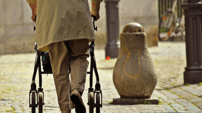 persona d'esquenes caminant pel carrer amb el suport d'un caminador