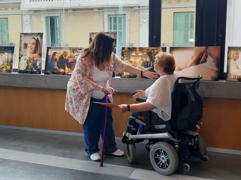 Dues dones amb discapacitat física i/o orgànica davant fotografies de l'exposició Dones diverses 