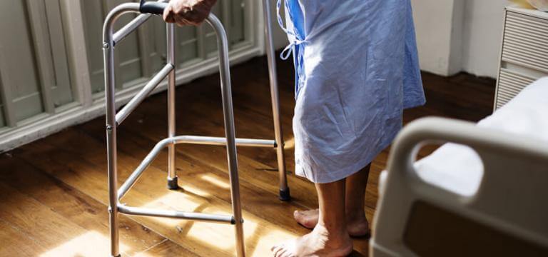 Un anciana de pie ante la cama ayudándose de un andador